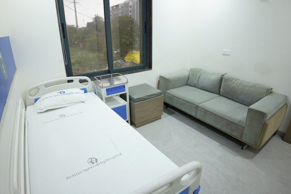 Hospital room featuring a bed, couch, and window, designed for patient care by a retina specialist doctor.